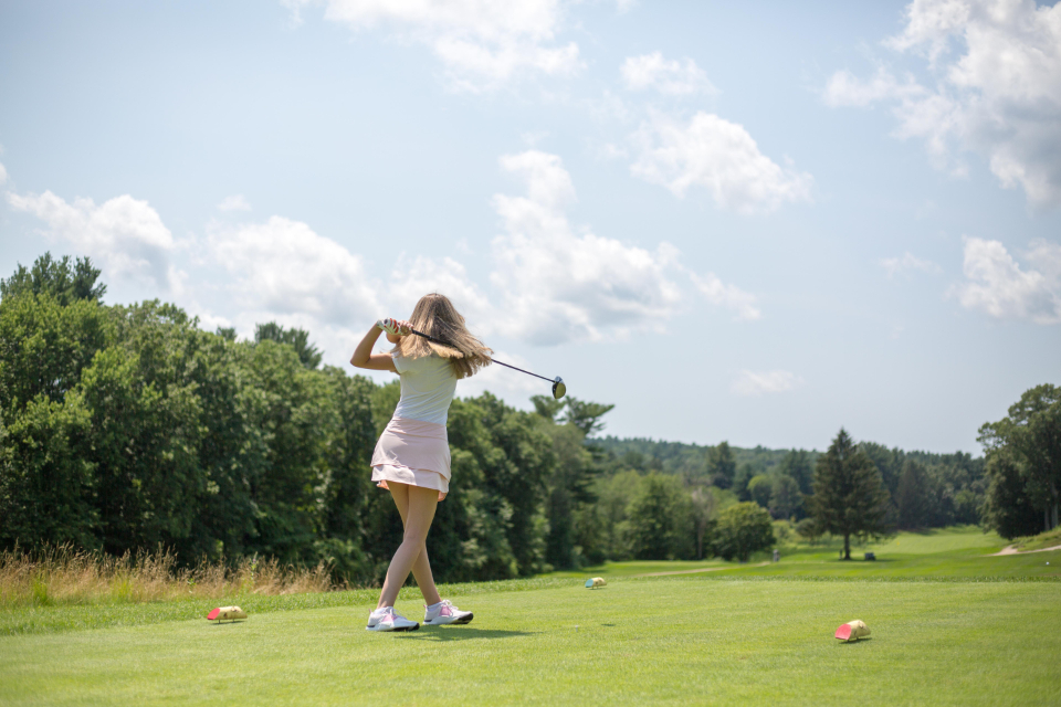 Golfer mid-swing on a tree-lined fairway